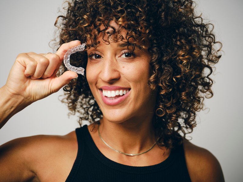 A woman holding an Invisalign retainer and smiling by Villanova Dental Studio