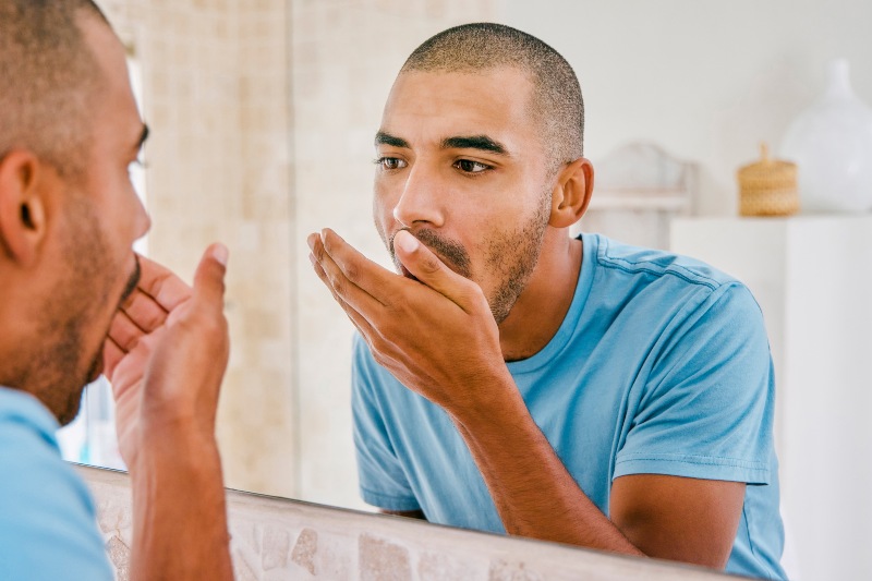 Man checking his breath in the mirror and covering his mouth due to bad breath (halitosis) concerns in Kanata and Stittsville, ON